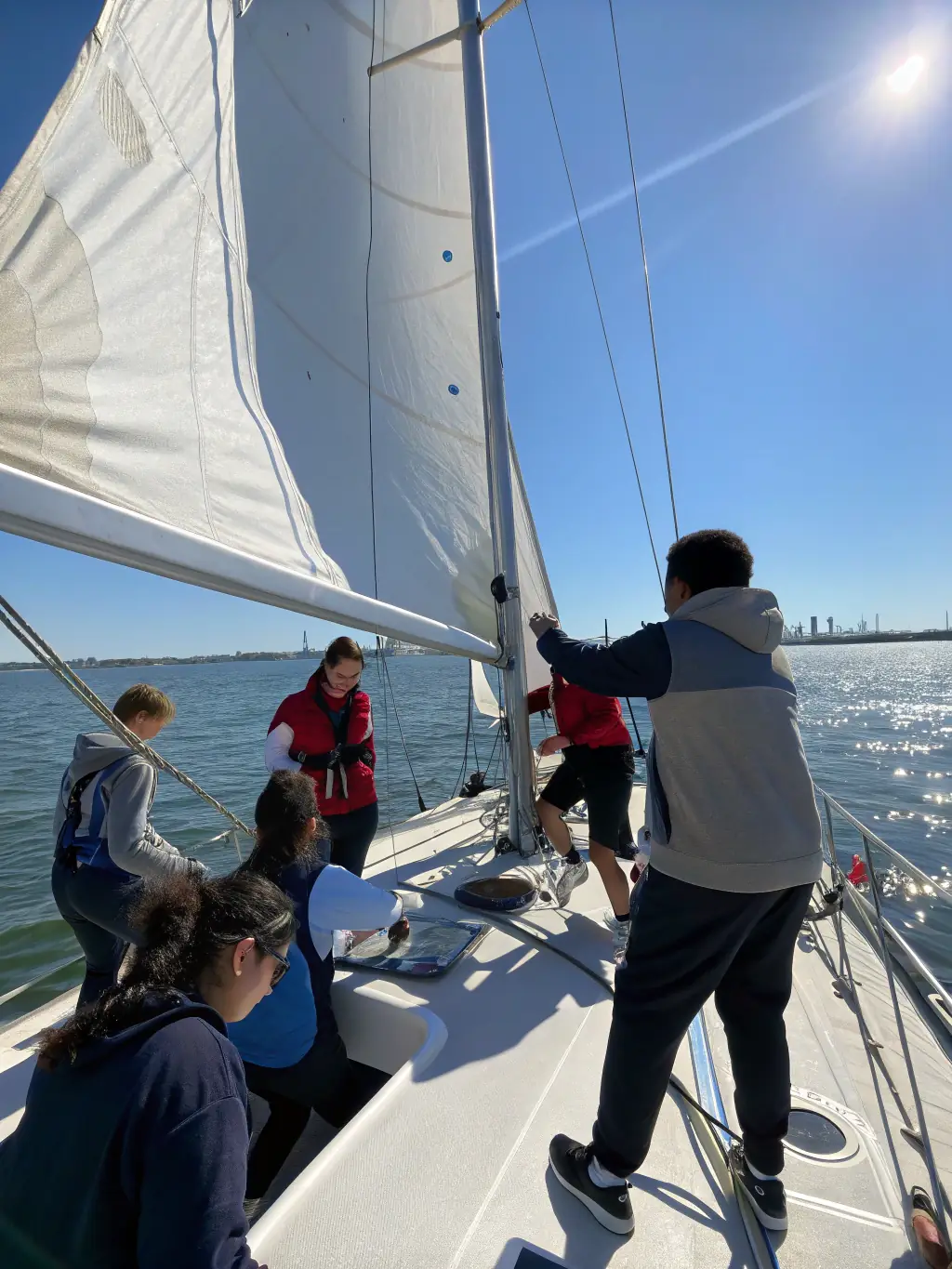 A group of diverse individuals learning basic sailing techniques on a small sailboat in a calm bay, under the supervision of an instructor, showcasing the introductory sailing program.